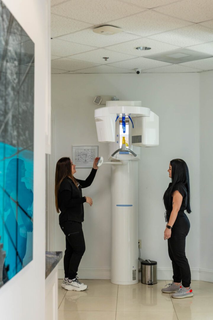 Two women using dental imaging machine.